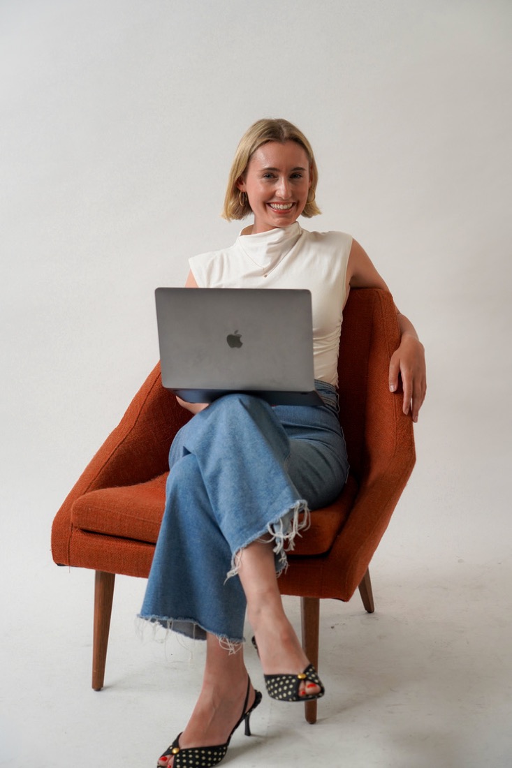 Anna smiling in an orange armchair with a laptop on her lap
