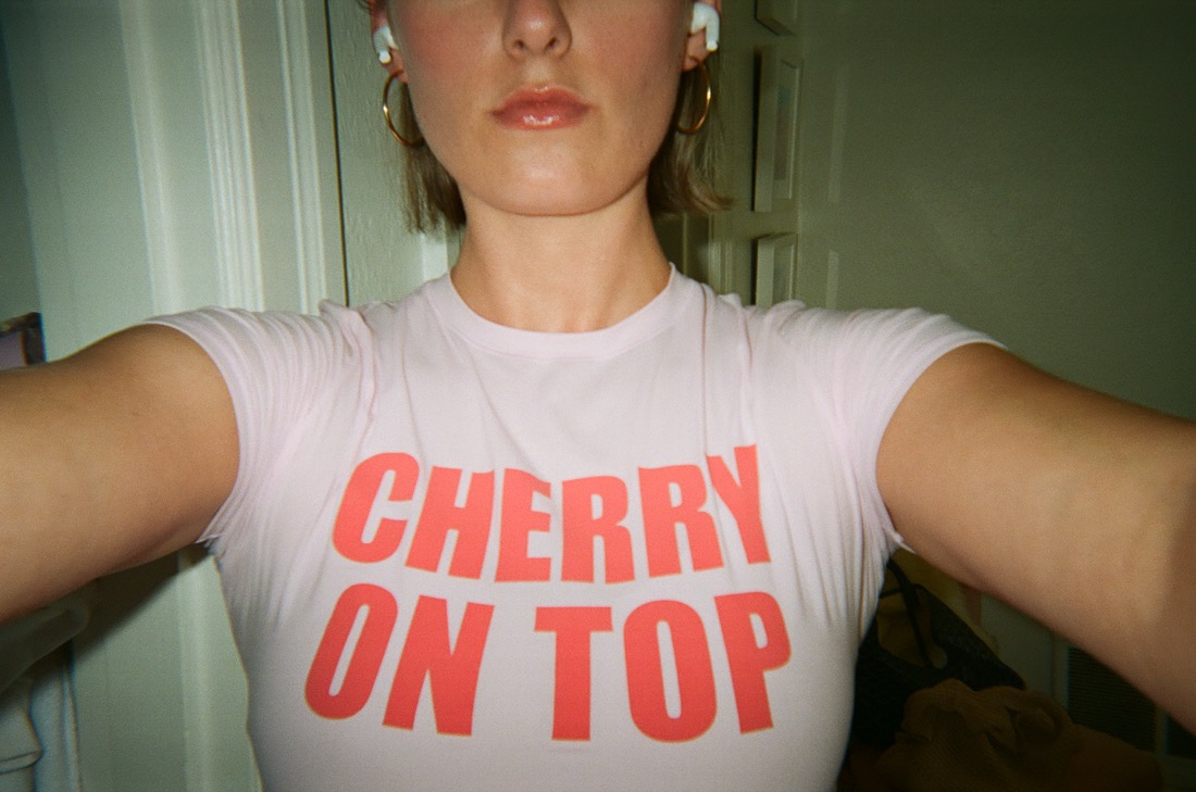 A film selfie of Anna in a pink t-shirt that says cherry on top