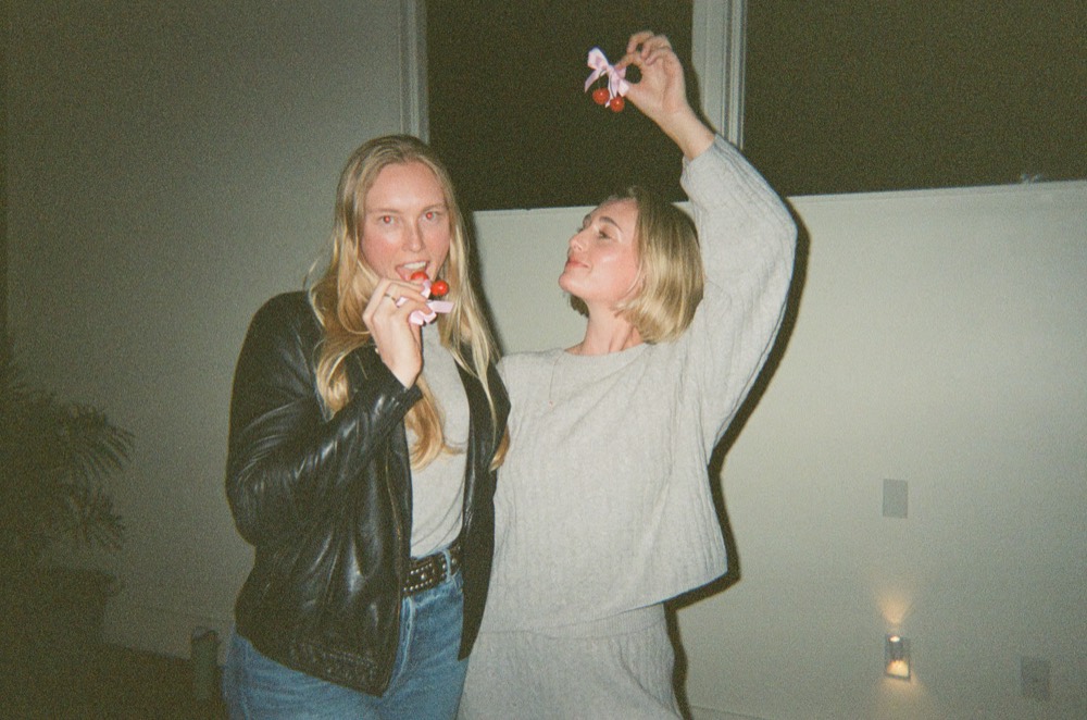 Two women messing about, holding up cherry charms tied with pink ribbon
