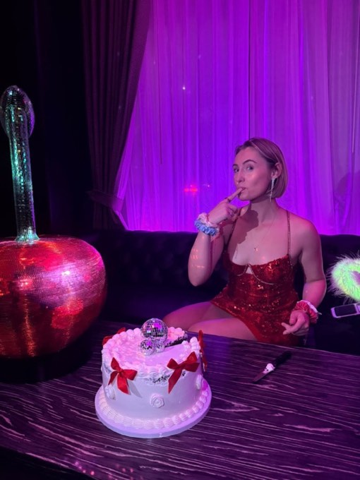 A woman in a red sequin dress beside a white cake topped with disco balls and a giant mirrored cherry