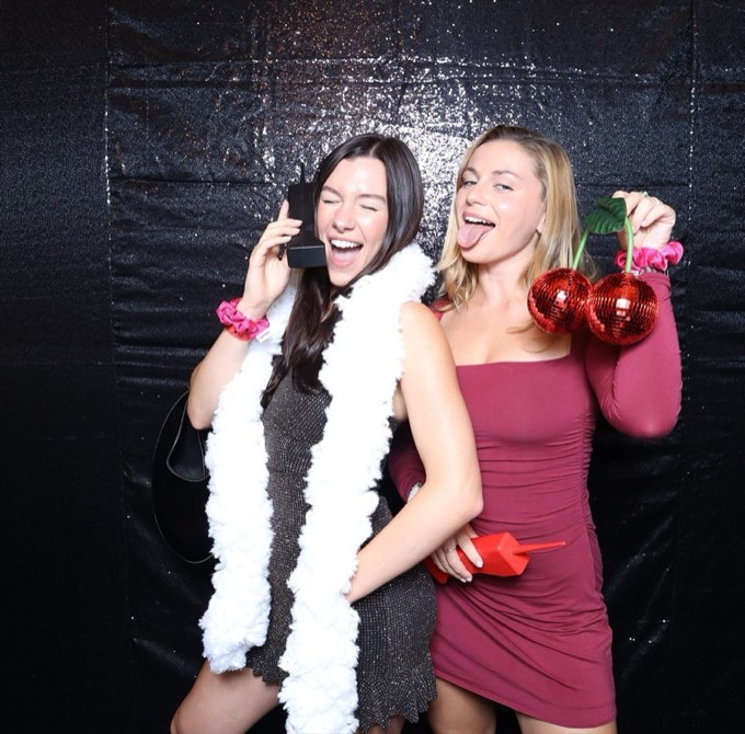 Two women in the photo booth, one on a giant prop phone, the other holding cherry disco balls
