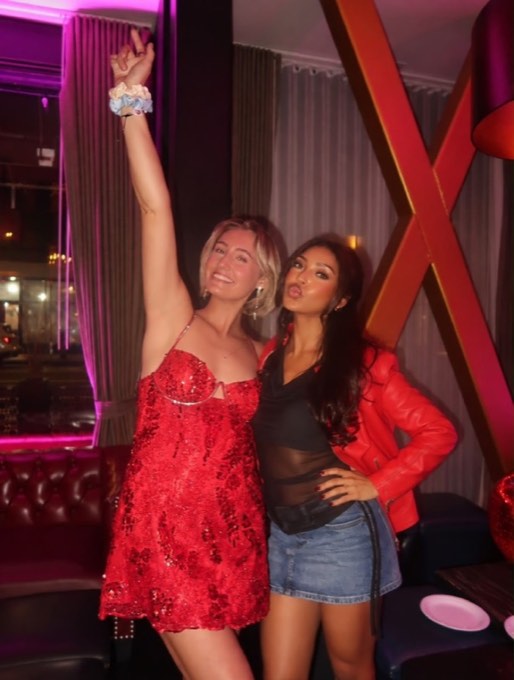 Two women posing in the venue under pink light, one in a red sequin dress, one in a red leather jacket