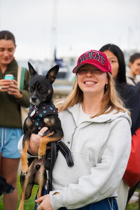 A woman in a red cap holding a small black dog on a Cherry walk